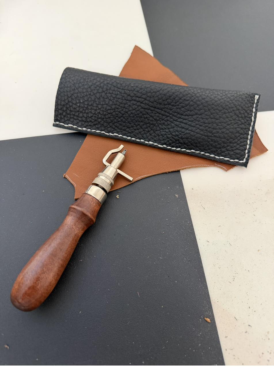 Black pebbled leather eyeglass case with a leatherworking tool