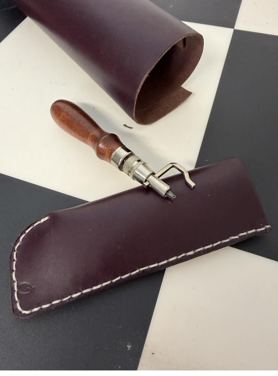 Rolled leather eyeglass case alongside a wood-handled leatherworking tool