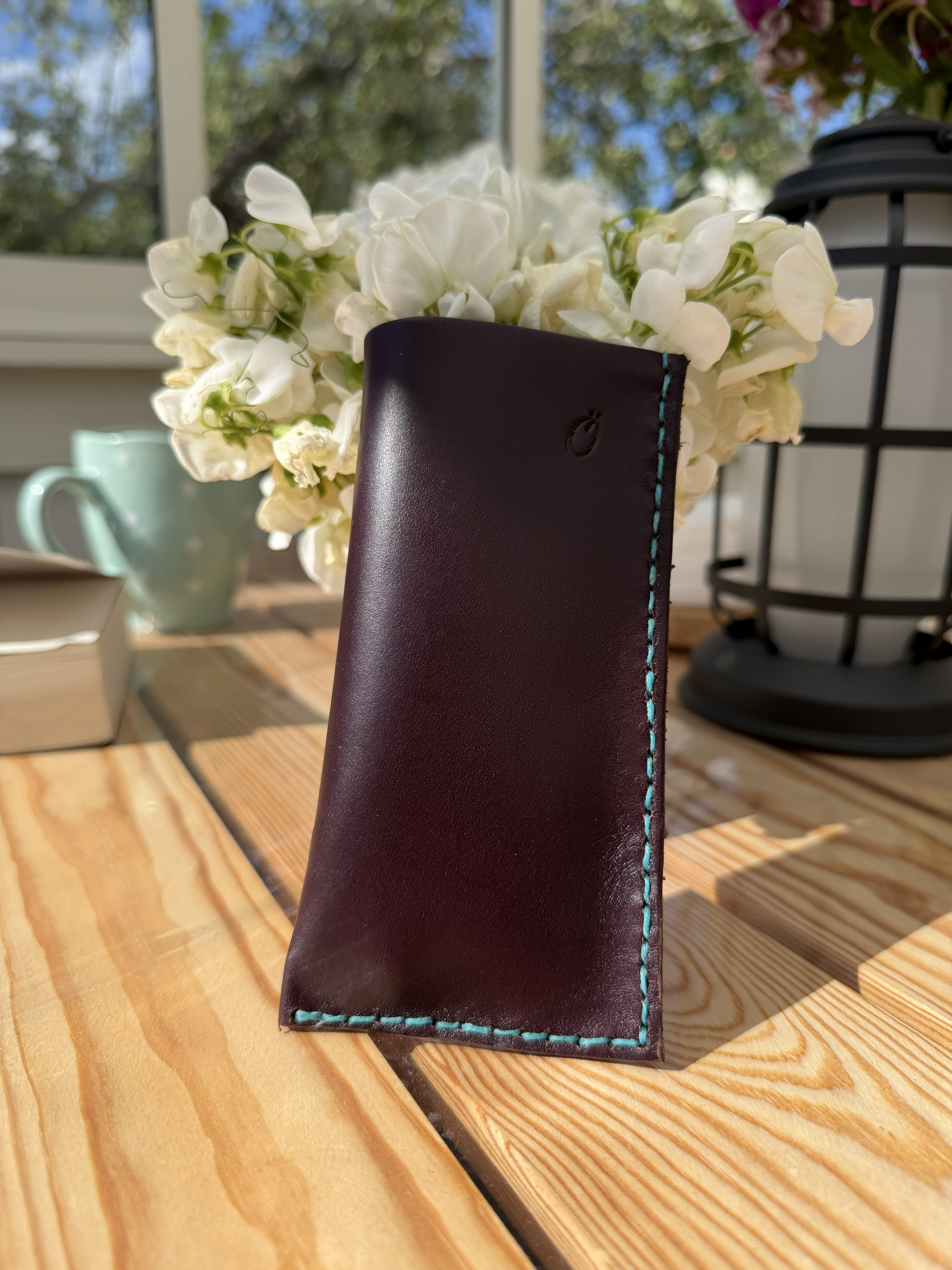 Slim oxblood leather eyeglass case with teal contrast stitching and stamped maker's mark